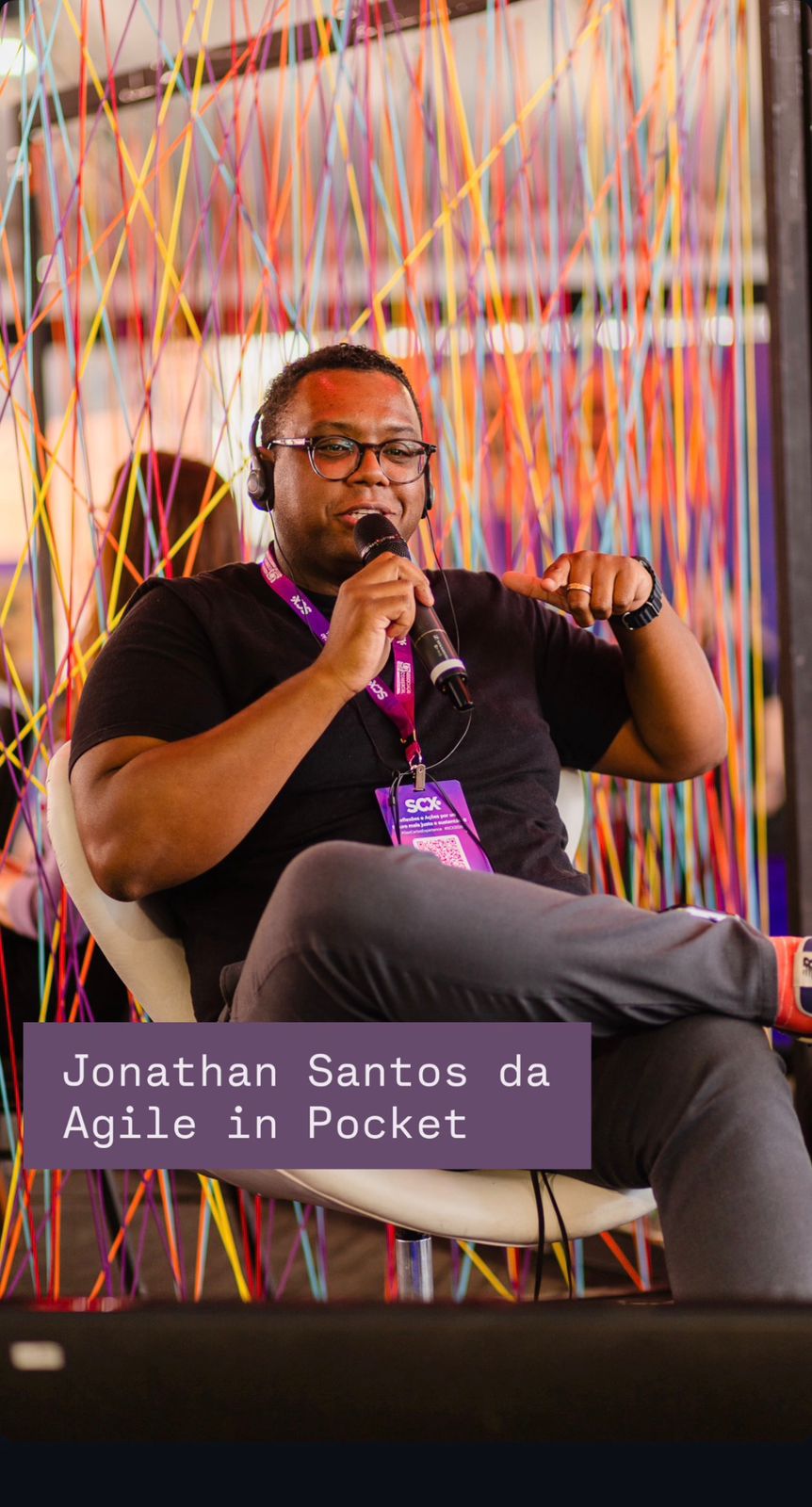 Jonathan Santos palestrando com microfone em um painel de tecnologia